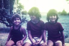 A brother and two sisters smile at the camera. The photo is faded and looks to be from the 1970s or early 1980s.