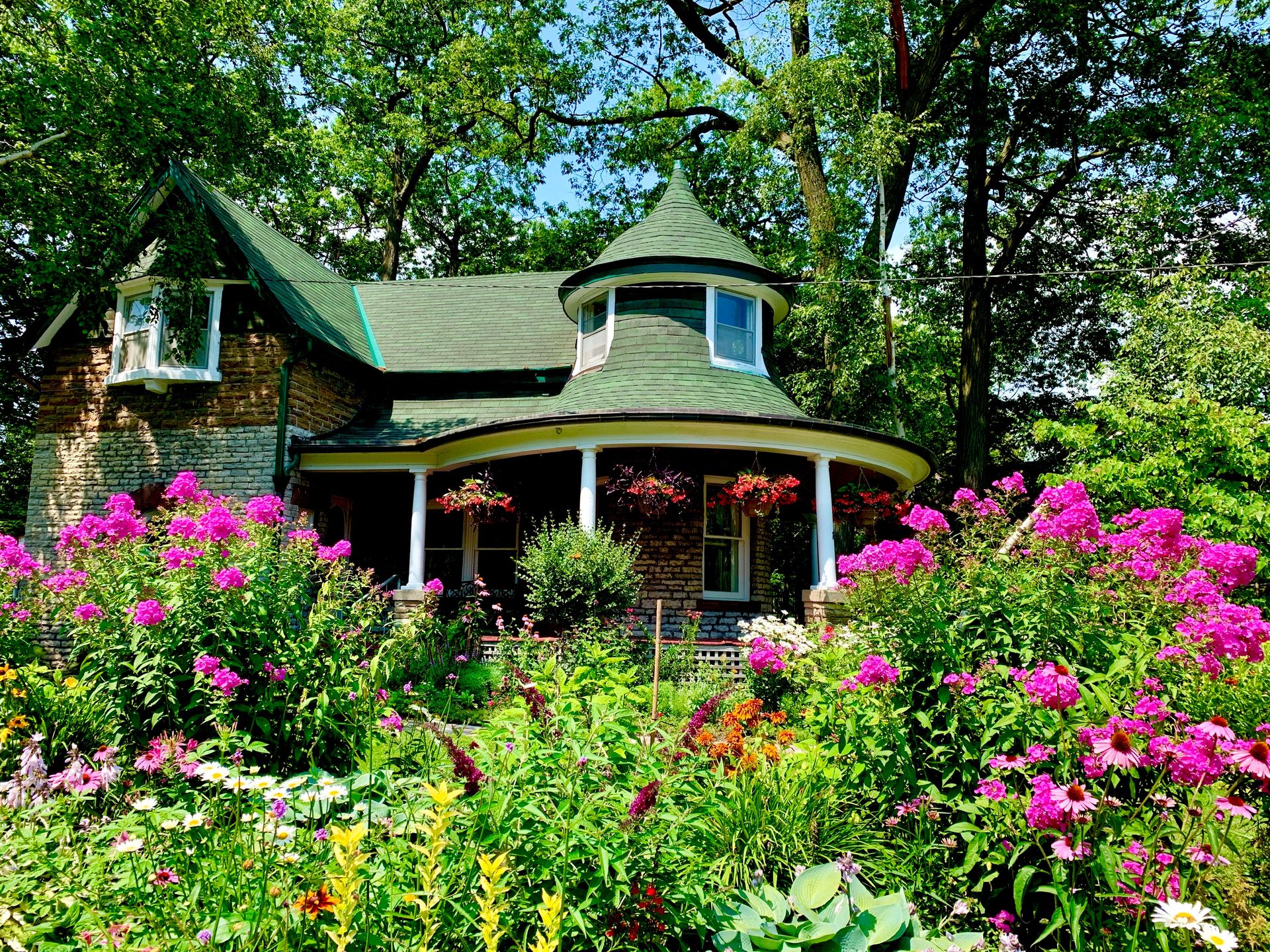 An example of south facing garden ideas showing a period house behind a large flower bed full of pink and yellow plants