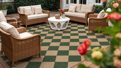 Green-and-neutral harlequin outdoor rug styled on a flower-lined outdoor patio with wicker garden furniture