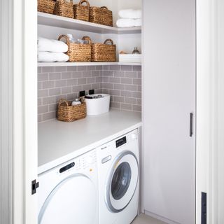 Washing machine and tumble dryer in white utility room with woven storage baskets