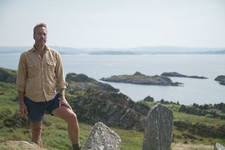 Ben Fogle standing on top of a hill with the sea in the background.