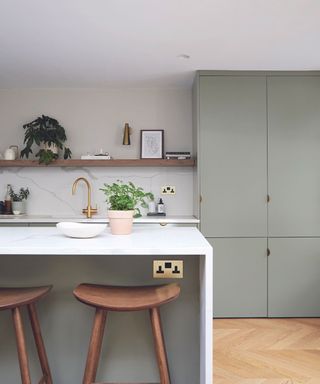 A kitchen with light green cabinets, a white kitchen island and wooden shelves