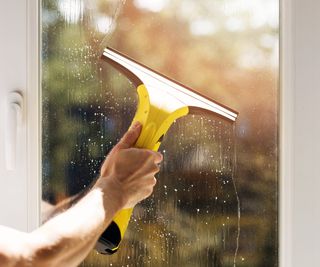 male hand using yellow window vacuum on window pane