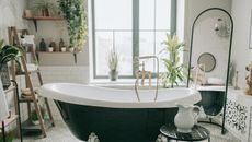 a bathroom with a green freestanding tub, a mirror in the background and plants all over and white walls