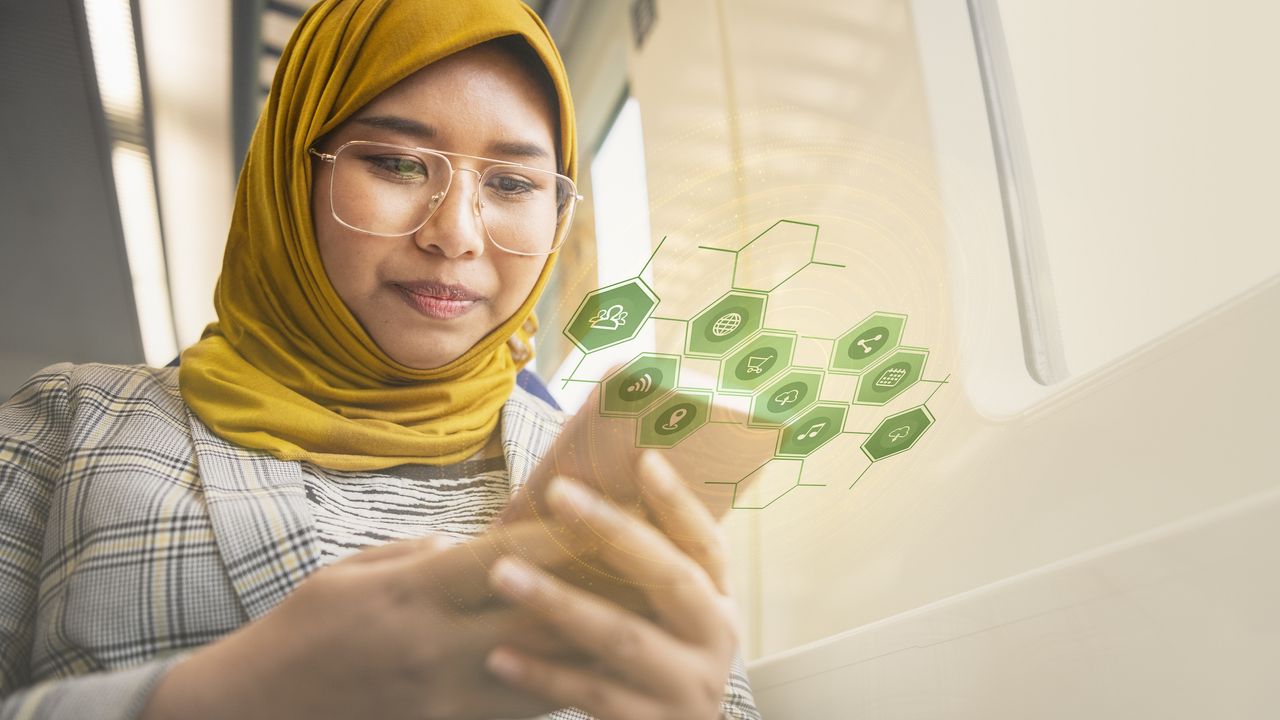 A woman uses her smartphone to check on her finances while green icons representing money and shopping and other things float around her phone.