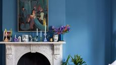 Living room with Bothy Blue by Farrow & Ball walls, marble fireplace decorated with candlesticks and candles on top, and an impressionist painting above.