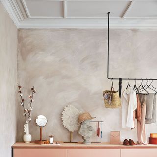 Dressing room area with limewashed walls and a pink storage unit with a mirror, clothes, and accessories on it