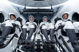 four astronauts in black-and-white spacesuits inside a SpaceX Dragon capsule.