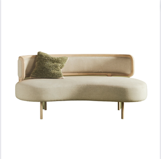 A curved cream linen sofa with a cushion 