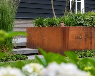 large corten steel planters, planted with a small tree, grasses and plants