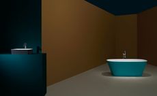 Interior room, deep turquoise, mustard yellow and rust coloured walls, deep turquoise exterior and white interior free standing bath tub, silver taps, grey and white wash basin on a deep turquoise square display unit, white floor