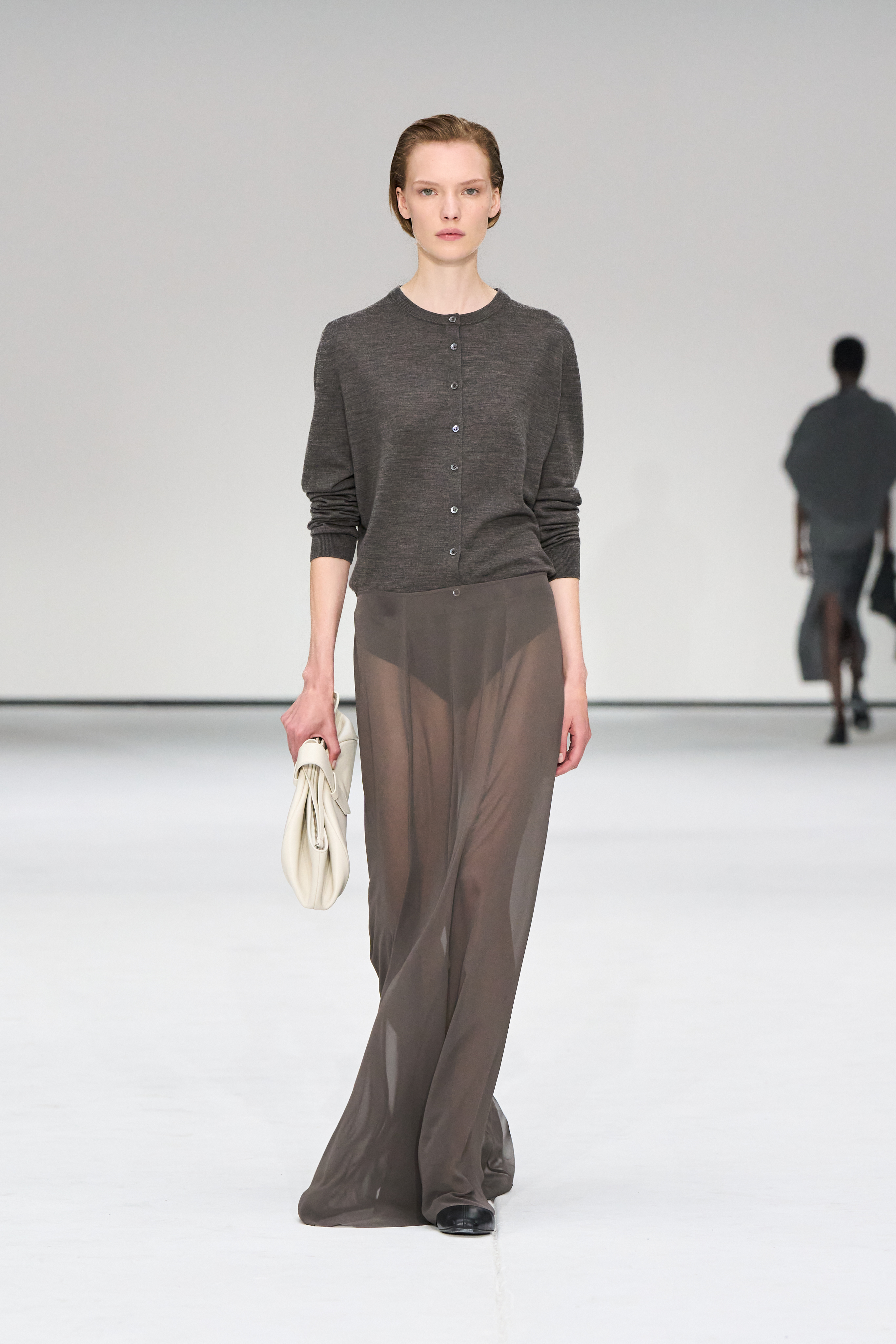A woman carries an oversize ivory clutch on the COS runway.