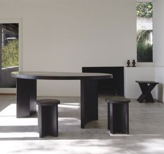 View of the dark wood 'Chene' desk and stools by Atelier de Troupe in a space with white walls and grey floors