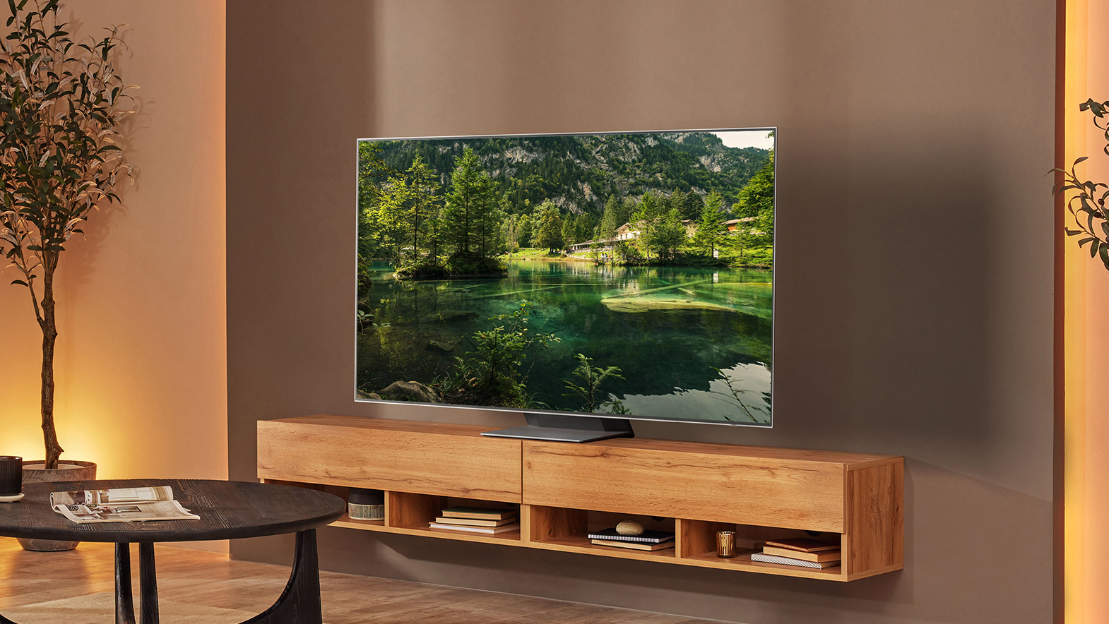 Samsung S95B en una sala de estar con muebles de madera, mostrando un paisaje verde en el televisor