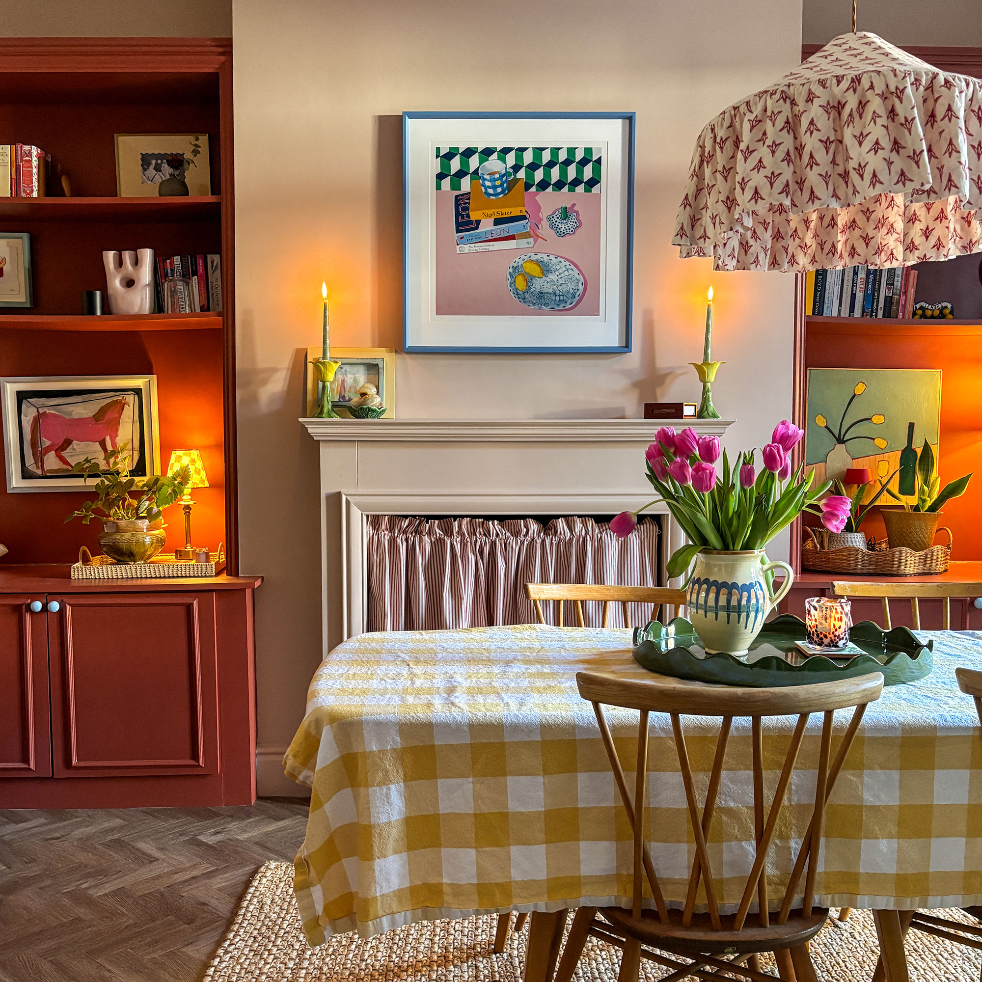 Dining room with neutral walls, terracotta built-in storage, art on walls, patterned lampshade on pendant light and table covered in yellow and white gingham tablecloth