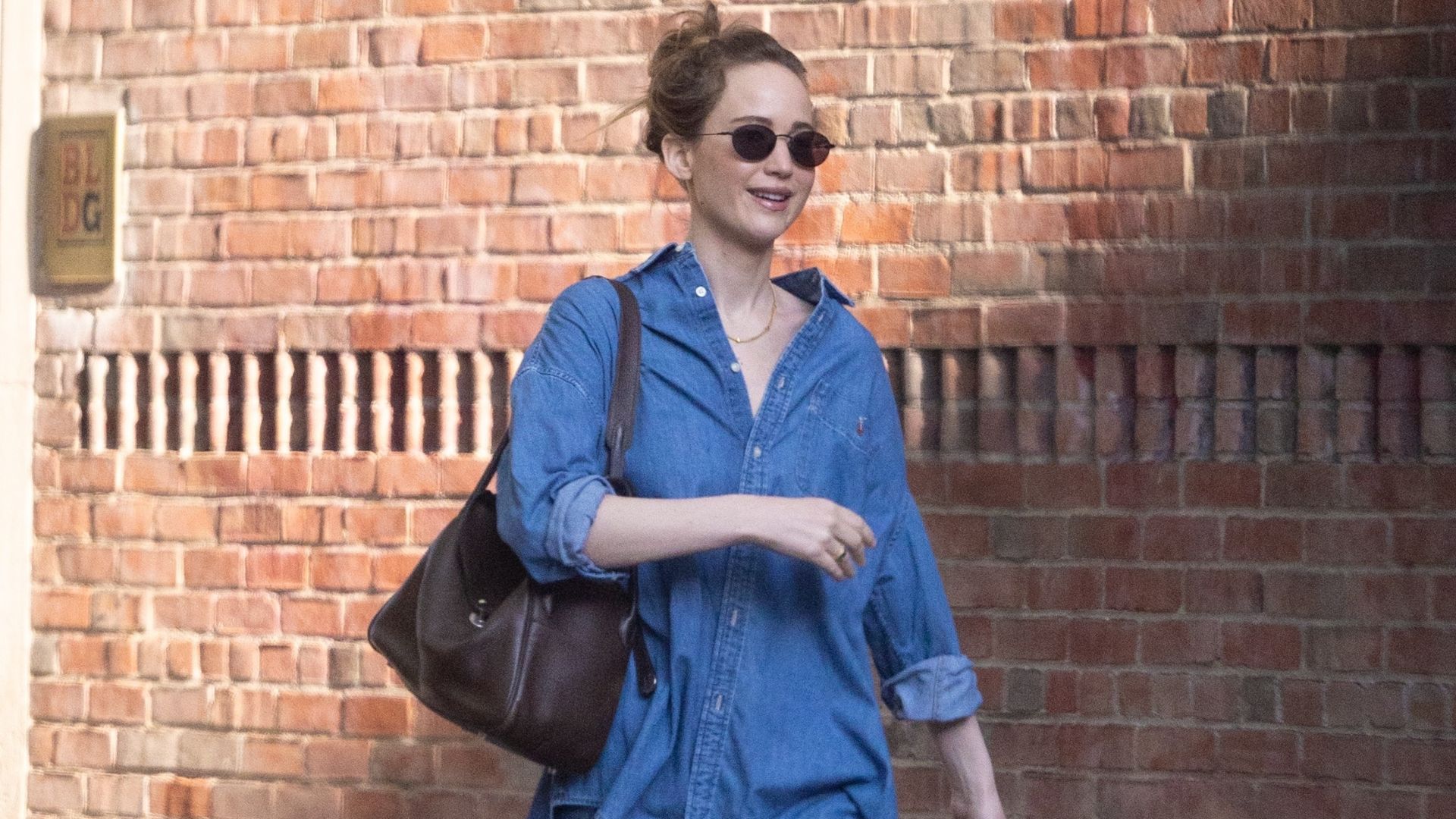 Jennifer Lawrence walks down the street in New York wearing baggy blue jeans with a denim skirt and bright blue shoes.