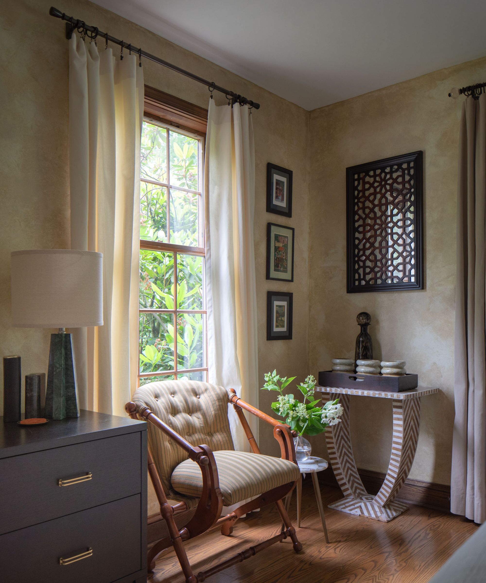 Living room with lime wash walls, large window with white curtains, antique armchair and console with decor