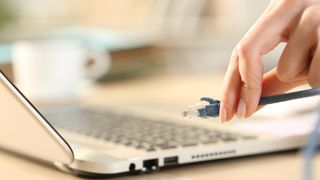 Close up of woman hands plugging ethernet cable on laptop on a desk