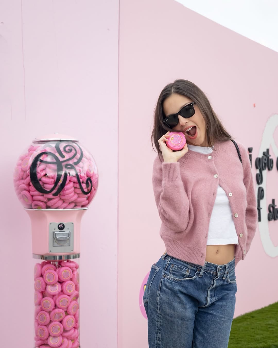 Olivia Rodrigo wears a pink Doen cardigan with blue jeans and a white T-shirt and carries a black woven bag