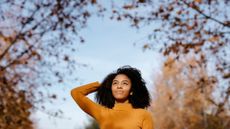 Thoughtful Afro woman with head in hand standing in park during autumn