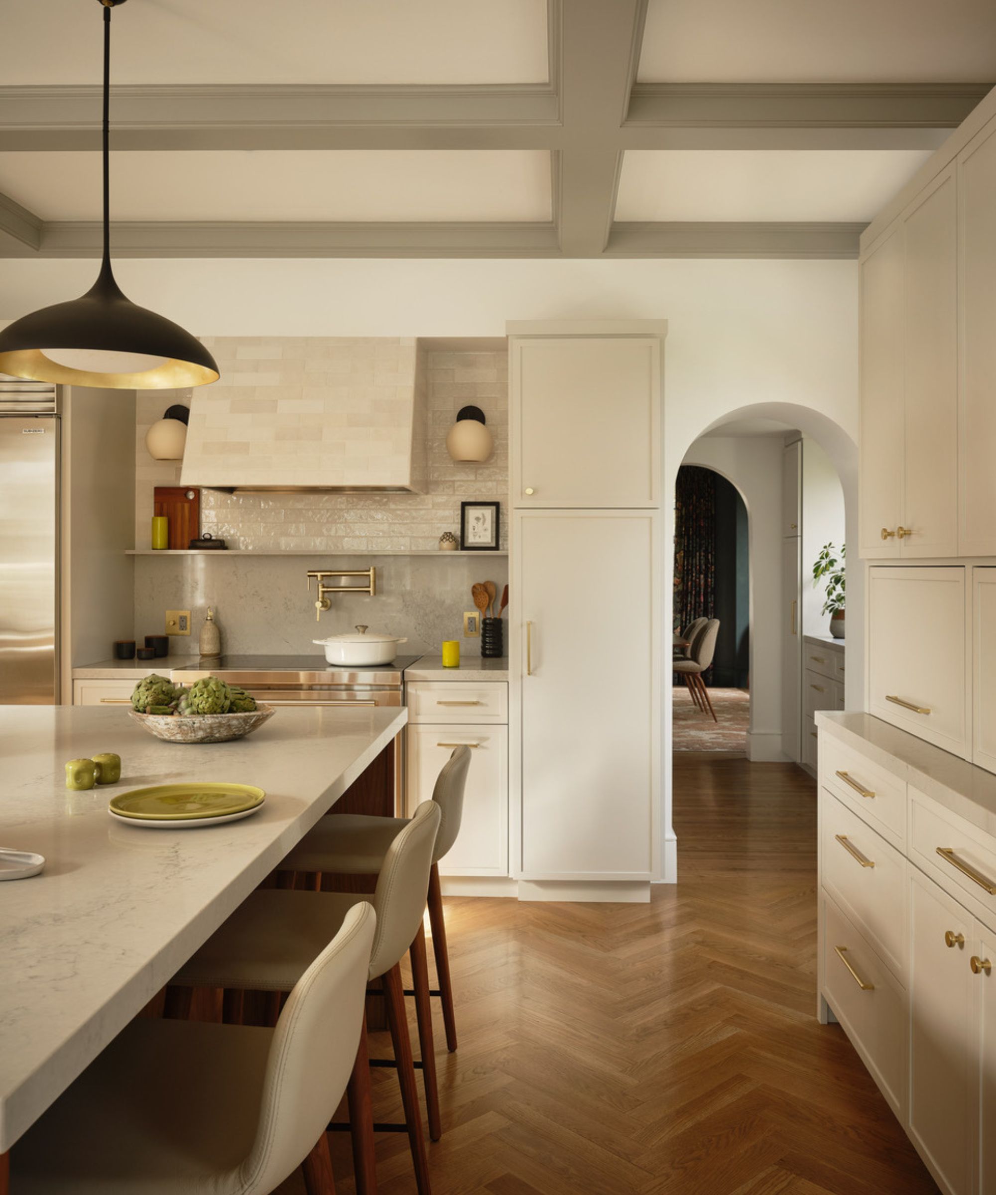 A neutral kitchen with warm white cabinets, marble countertops, and a tiled backsplash that continues over the range hood