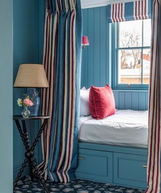 Sky blue painted bedroom nook with striped curtain and wooden side table