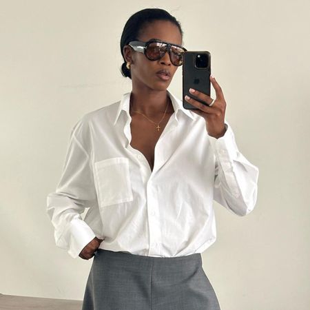 Woman taking mirror selfie, wearing white button-down shirt and orange oversized sunglasses