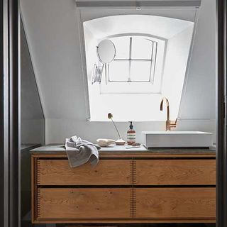 bathroom with white washbasin with brass tap angled window and mirror