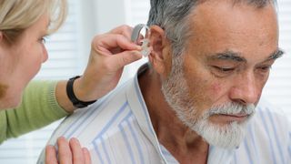 A woman fits an older man for a hearing aid