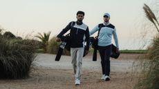 Two golfers walking while carrying their bags