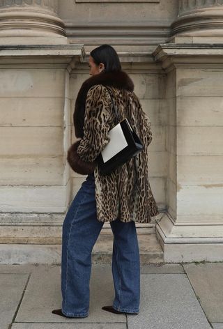 The frame bag trend is shown in a street-style photo of a woman wearing a leopard print coat with wide-leg jeans, black pointed pumps, and a black and white frame bag