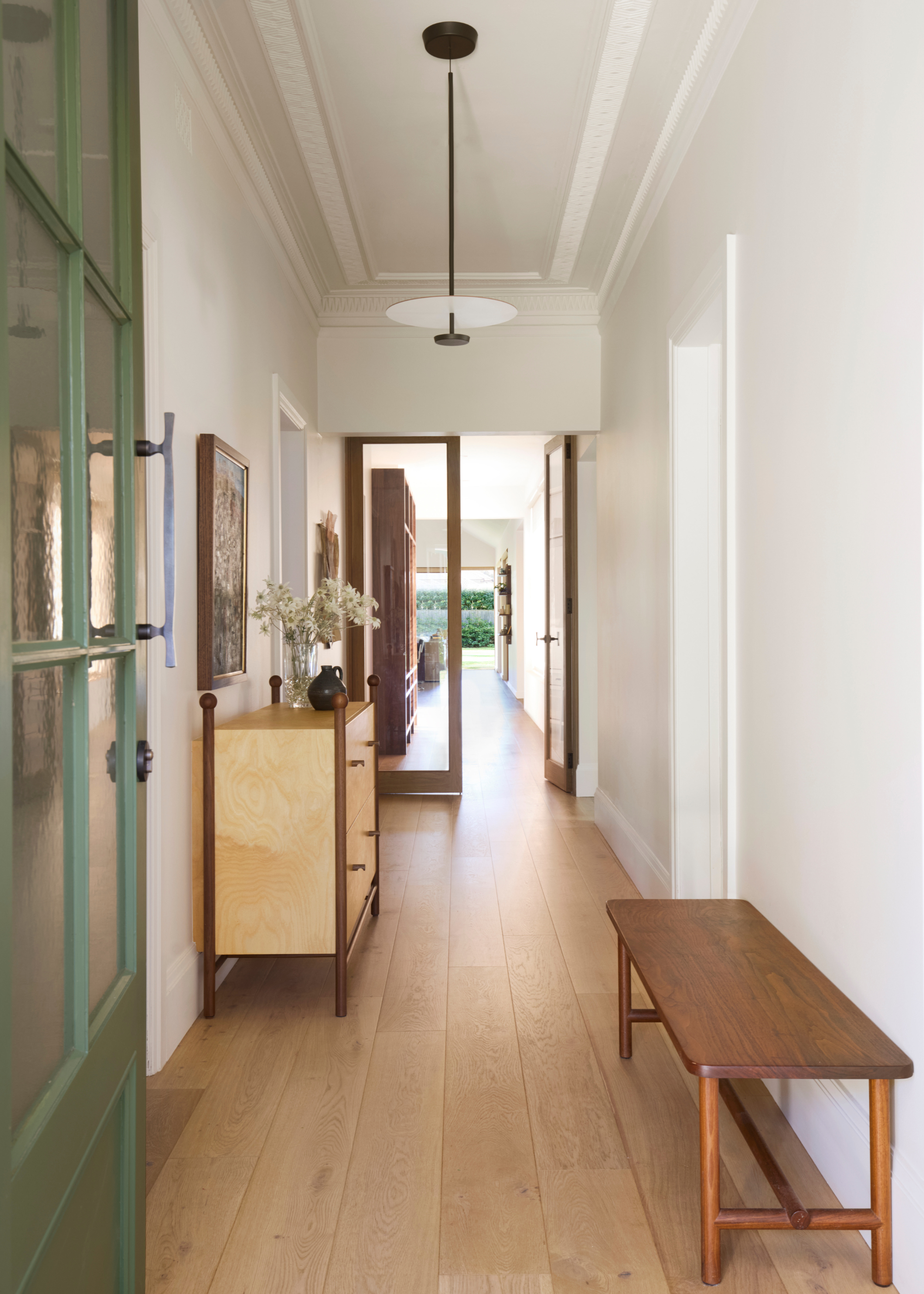 A white entryway with a wood bench, a wood sideboard, a white light and a green door with a blue handle