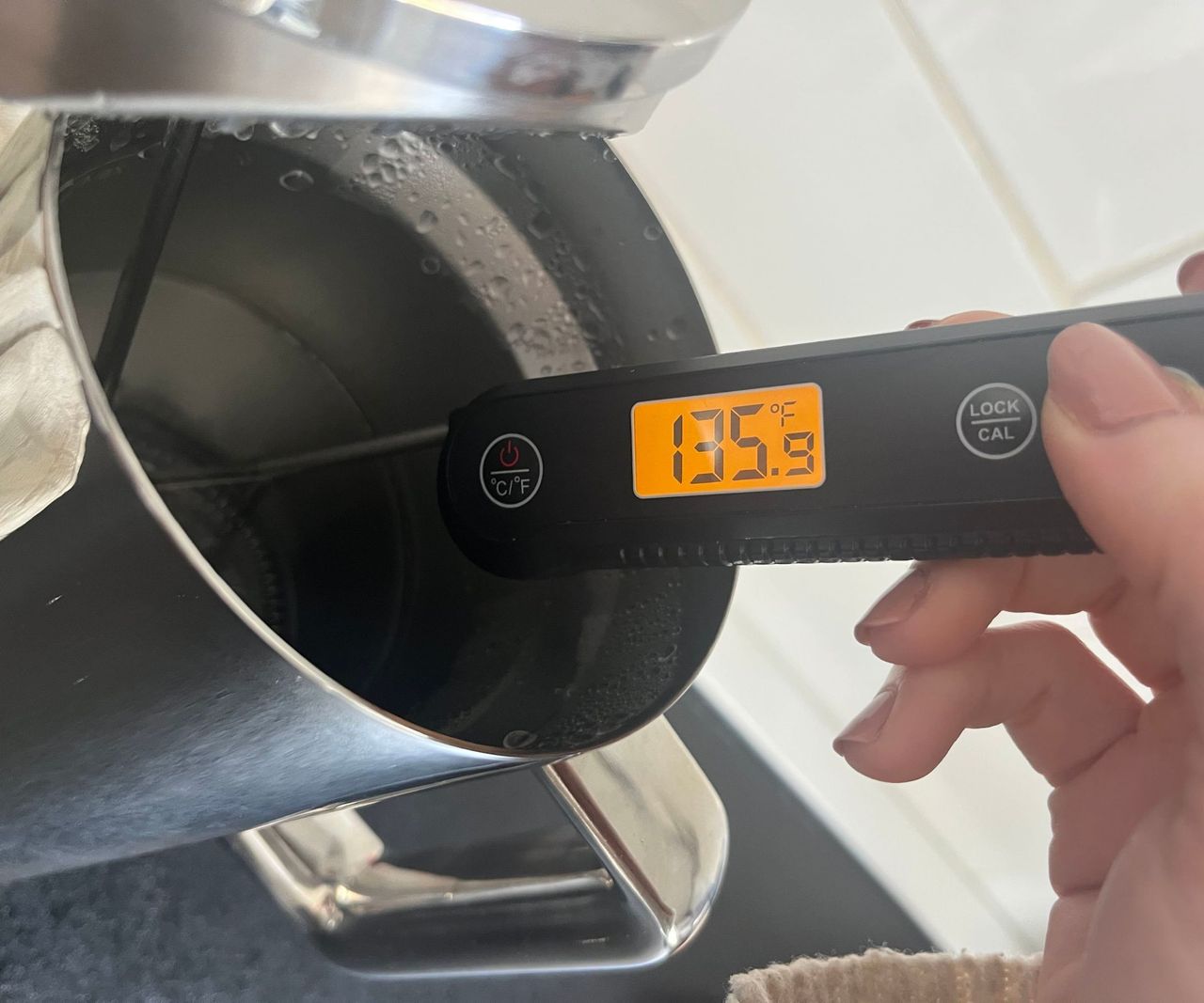 a digital thermometer reading the temperature of water in a stainless steel coffee press. It shows 135F