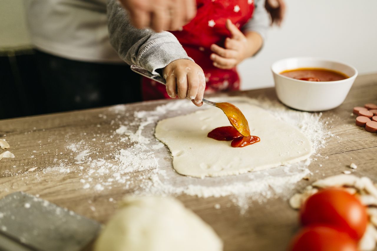 Father and son preparing pizza dough together.