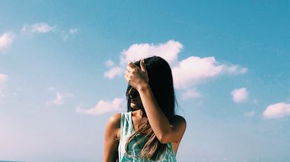 A woman is seen With Hand In Hair Standing Against Sky