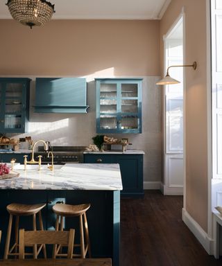 blush / coral kitchen with teal cabinetry, marble countertops, wooden floor boards, wooden stools, brass taps, chandelier, wall light