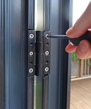 a screwdriver tightening screws in a bifold door hinge