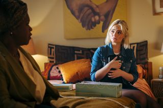 Doctor Who: Ruby Sunday (Millie Gibson) sits on her mum's bed, with an open shoebox in front of her. Ruby is clutching something from inside the box to her chest, as her mother Carla (Michelle Greenidge) - visible in the foreground but out of focus - is talking to her