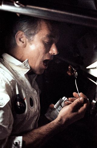 Astronaut Eugene A. Cernan holds some food on a spoon close to his open mouth.