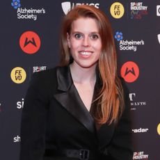 Princess Beatrice smiling wearing a black blazer dress on a red carpet