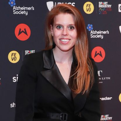 Princess Beatrice smiling wearing a black blazer dress on a red carpet