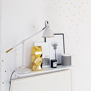 White radiator with white floating shelf above it, with desk lamp and accessories