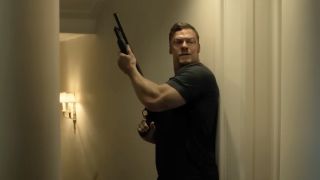 Alan Ritchson as Jack Reacher sneaking past a corner with a shotgun on Reacher