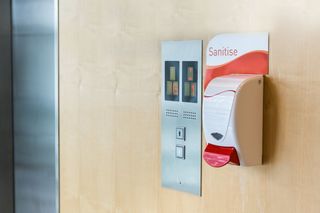 A hand sanitizer dispenser next to an elevator.