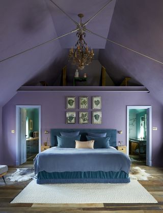 lilac bedroom with vaulted ceiling, doors off to his and hers bathrooms, teal bedding, artwork above headboard, chandelier, lilac ceiling and walls, hardwood floor, rugs