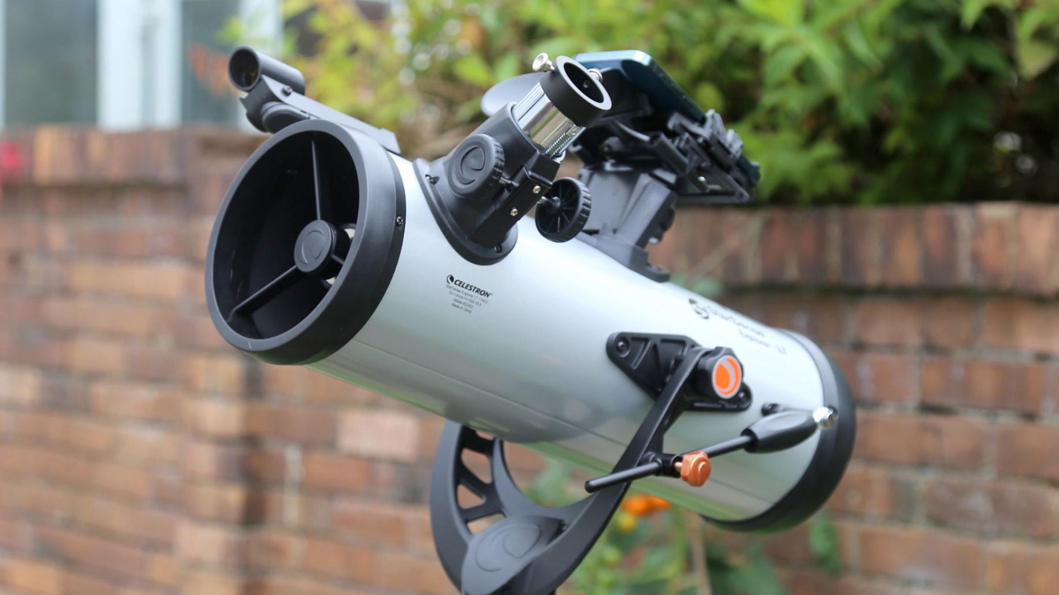 Celestron StarSense Explorer LT 114AZ pointing at the sky against a brick wall backdrop