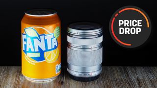 An Olympus M.Zuiko 40-150mm f/4.0-5.6 R lens next to a can of Fanta, with the text "Price drop"