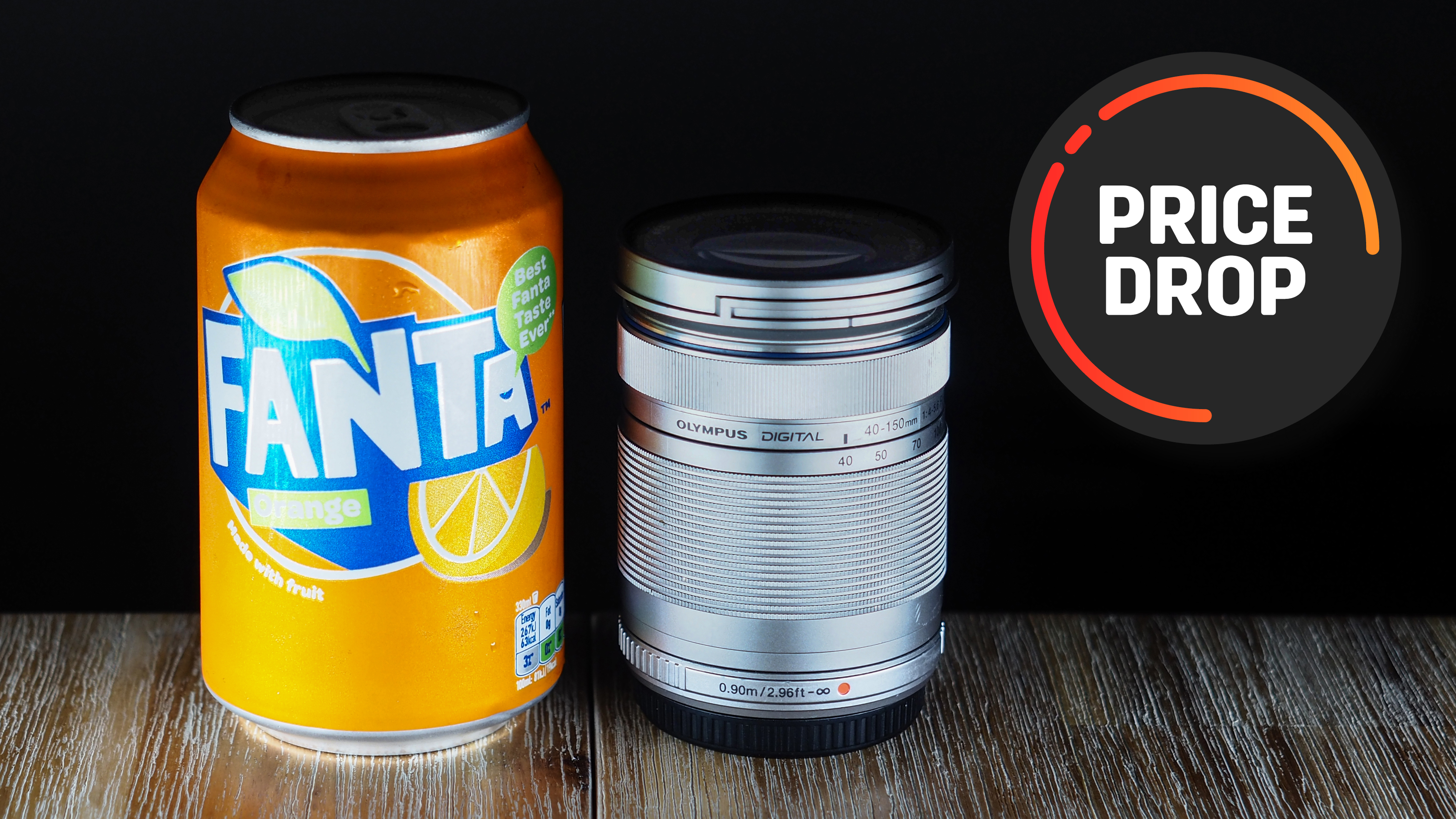 An Olympus M.Zuiko 40-150mm f/4.0-5.6 R lens next to a can of Fanta, with the text "Price drop"