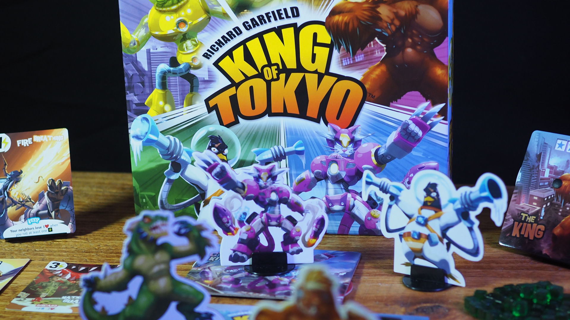 King of Tokyo components, box, and cards on a wooden table against a black background