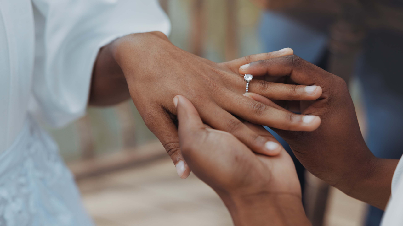 Close up of twe people&#039;s hands as one places a diamond ring on the other&#039;s